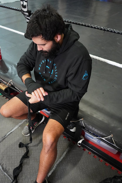 Man sitting down, wrapping his knuckles before boxing. He is wearing the Collective Hoodie in Black. 