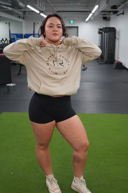 Woman standing wearing the Collective Hoodie in Tan