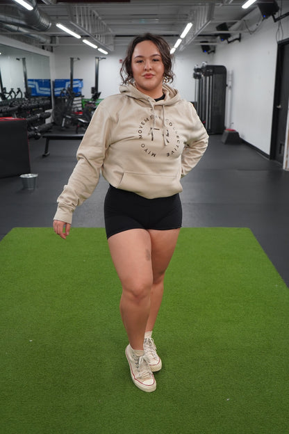 Woman standing wearing the Collective Hoodie in Tan