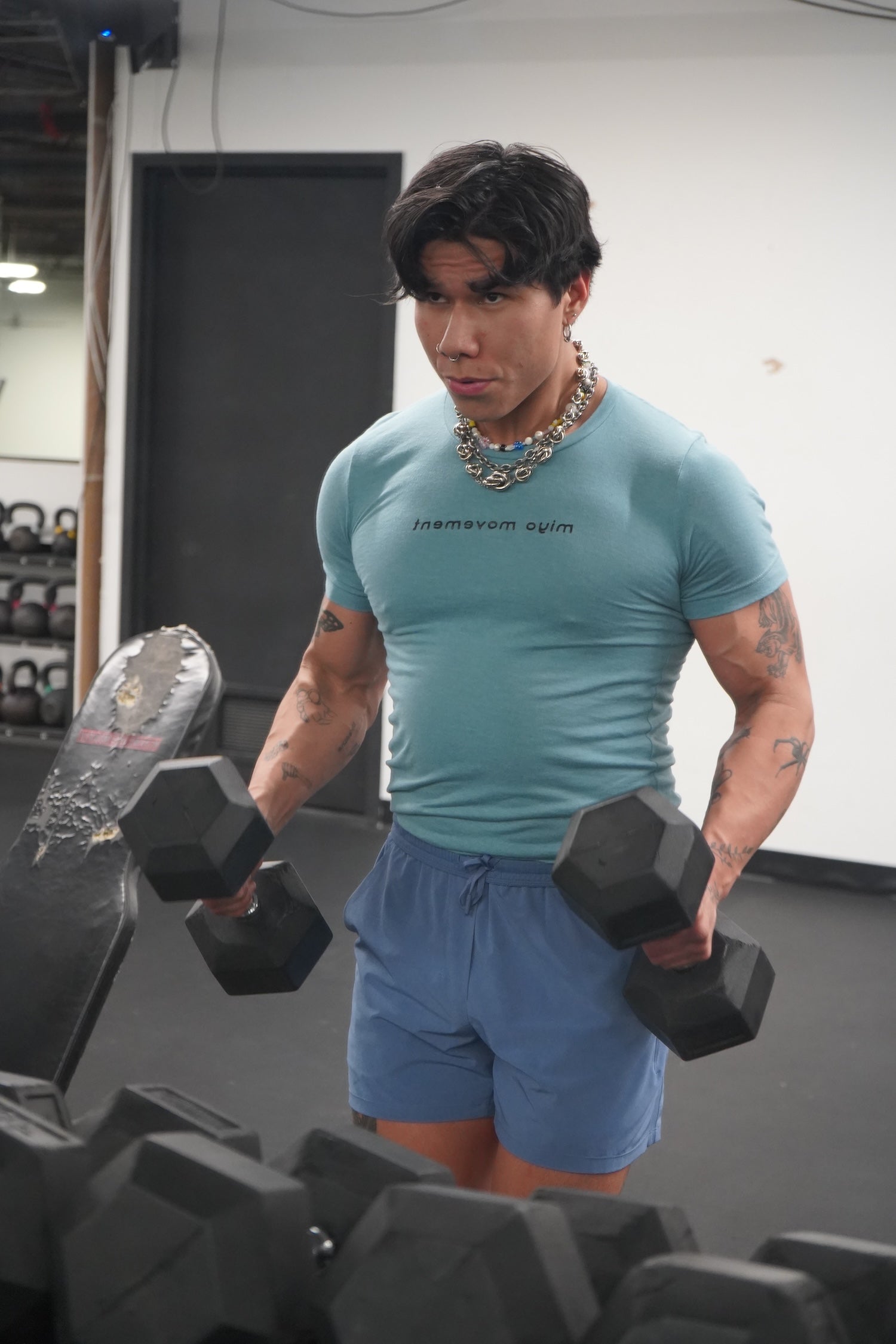 Man lifting dumbbells, wearing a Blue Lagoon Movement T-shirt